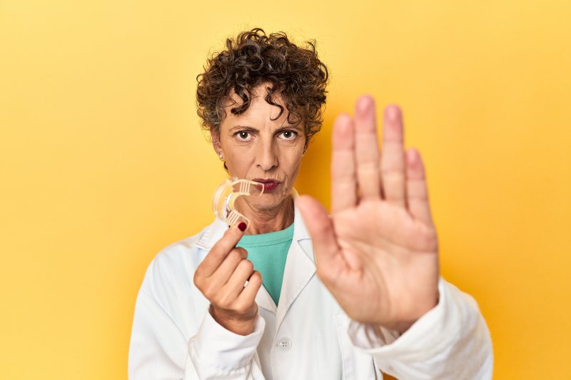 A dentist holding a clear aligner in one hand while using the other as a stop sign